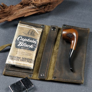 Pu&ograve; includere: Una custodia in pelle marrone per tabacco con chiusura a zip. La custodia ha due scomparti, uno per un pacchetto di sigarette Captain Black Gold e l'altro per una pipa di legno. La custodia ha anche un cinturino in pelle verde.