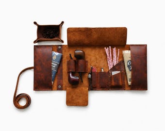 Può includere: Un astuccio per pipa in pelle marrone, aperto per mostrare il suo contenuto. L'astuccio include un vassoio per tabacco, due pipe, una custodia e altri accessori. La pelle è di un ricco colore marrone caldo e l'astuccio è progettato per essere portatile.
