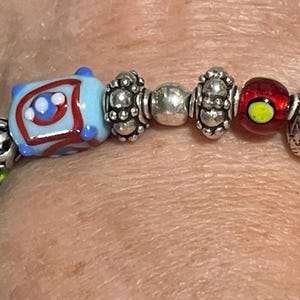 May include: A colorful beaded bracelet featuring a variety of glass beads in blue, red, black, and silver. The beads have intricate designs and patterns, creating a unique and eye-catching accessory.