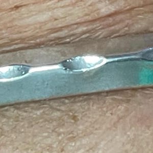 May include: A silver-toned metal bracelet with an open design. The bracelet features a series of oval cut-outs along its length. The edges are slightly beveled, and the overall appearance is sleek and modern.