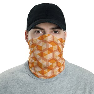 May include: A person wearing a black cap and a face covering with a geometric pattern of orange and beige squares and triangles.