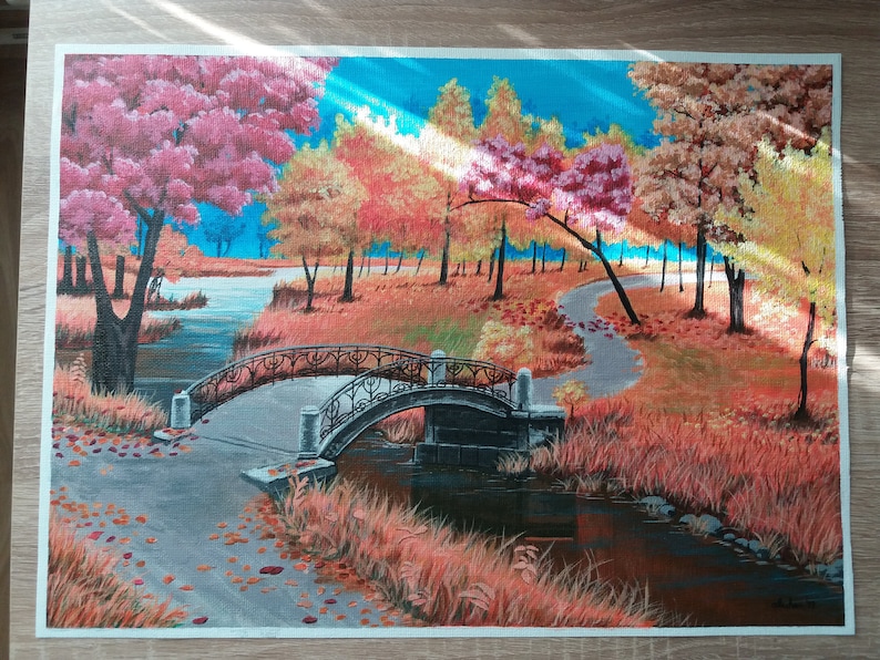 May include: A painting of a bridge over a stream in a forest. The trees are in autumn colors, with shades of red, orange, yellow, and brown. The bridge is made of stone and has a black metal railing. The stream is surrounded by tall grass and reeds.
