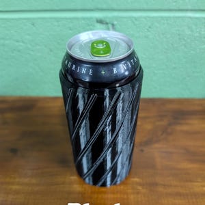 Pu&ograve; includere: Un portabevande nero a spirale con bordo argentato, che contiene una lattina di bevanda. La lattina ha testo verde e bianco. La parola "Black" &egrave; stampata in basso.
