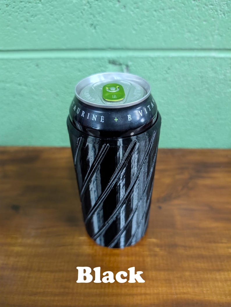 Pu&ograve; includere: Un portabevande nero a spirale con bordo argentato, che contiene una lattina di bevanda. La lattina ha testo verde e bianco. La parola "Black" &egrave; stampata in basso.
