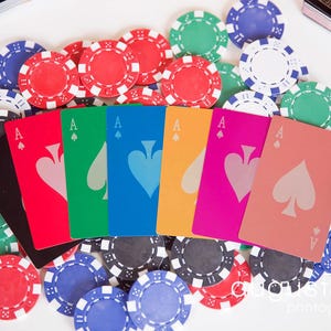 May include: A collection of poker chips in red, green, blue, and black surround a fan of playing cards. The cards are the Ace of Spades in various colors, including black, red, green, blue, yellow, pink, and peach.