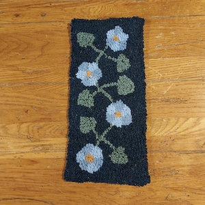 May include: A blue and green rug with a floral design. The rug has a dark blue background with light blue flowers and green leaves.