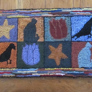 Puede incluir: Una alfombra colorida con un diseño de patchwork que presenta varias imágenes, incluyendo una estrella, un gato, un pájaro, un tulipán y una flor azul. La alfombra está hecha de lana y tiene un borde con flecos.