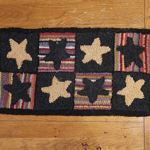 Puede incluir: Una alfombra de lana negra y marrón con un diseño de patchwork que presenta estrellas y un patrón geométrico. La alfombra está hecha de lana y tiene un aspecto cosido a mano.