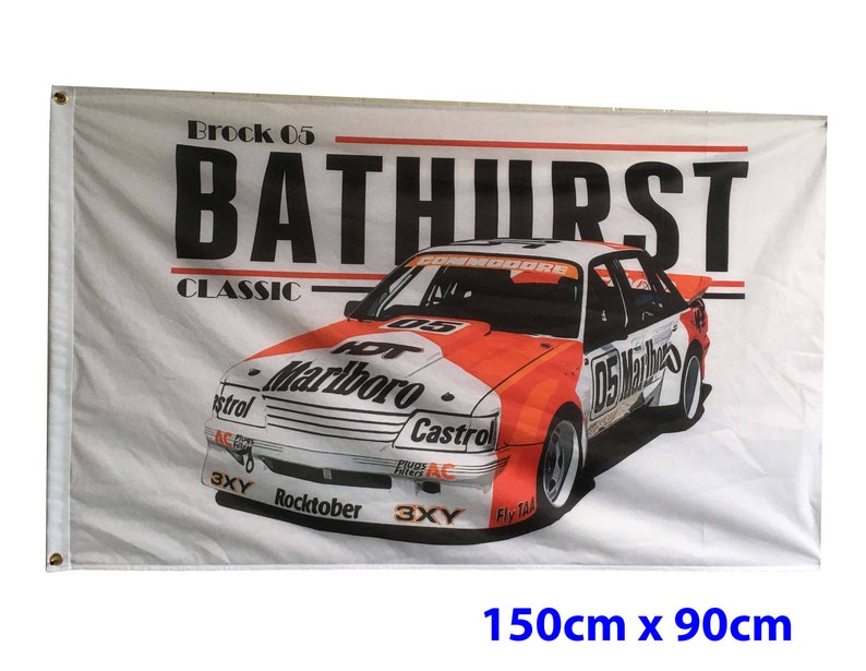 May include: A white flag with red and black text that reads "Brock 05 Bathurst Classic". A red and white race car with the number 05 and the words "Hot Marlboro" and "Castrol" is printed on the flag. The flag measures 150cm by 90cm.