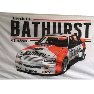 May include: A white flag with a red and white race car on it. The car is a Holden Commodore with the number 05 on the side. The car is sponsored by Marlboro and Castrol. The flag also has the text "Brock 05 Bathurst Classic" on it.