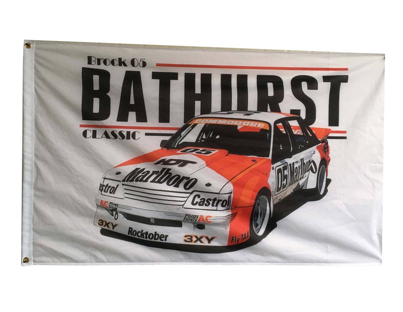 May include: A white flag with a red and white race car on it. The car is a Holden Commodore with the number 05 on the side. The car is sponsored by Marlboro and Castrol. The flag also has the text "Brock 05 Bathurst Classic" on it.