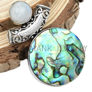 May include: A silver pendant featuring a round abalone shell inlay and a smaller round moonstone. The pendant has an ornate design and is ideal for jewellery making.