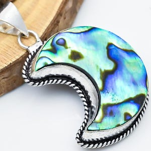 May include: A crescent-shaped pendant with a silver bail. The pendant features a polished abalone shell with iridescent blue, green, and purple hues, set in a silver frame with a twisted rope design.