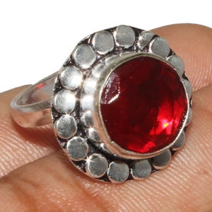 以下が含まれることがあります： 円形のテクスチャ加工されたベゼルにセットされた、大きな赤い宝石が付いたシルバーリングです。