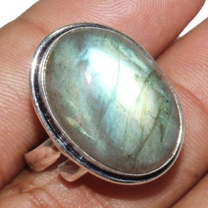 Puede incluir: Un anillo de plata con una gran piedra ovalada de labradorita. La piedra preciosa es de color azul verdoso con destellos iridiscentes.