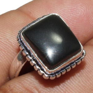 Puede incluir: Un anillo de plata con una piedra cuadrada negra engastada en un engaste de plata. El anillo tiene un borde con cuentas.