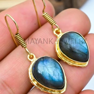 May include: A pair of gold-tone earrings featuring teardrop-shaped labradorite stones. The stones have a dark blue and green iridescent sheen.