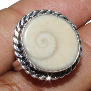 Puede incluir: Un anillo de plata con una incrustación de concha blanca. La concha tiene un patrón en espiral.