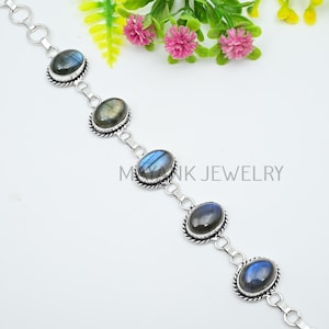 May include: A silver bracelet featuring oval-shaped labradorite stones. Each stone is set in a decorative bezel and connected by small silver links. The bracelet is displayed on a white surface with the text "MAYANK JEWELRY".