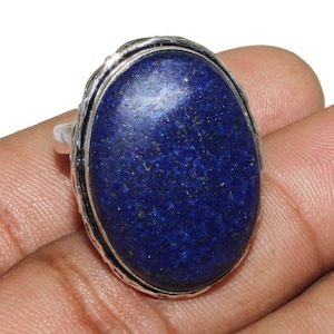 May include: A silver ring featuring a large oval lapis lazuli gemstone. The stone is a deep blue colour with gold flecks.