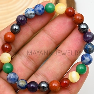 Puede incluir: Una pulsera de cuentas con piedras preciosas de colores. La pulsera incluye cuentas rojas, naranjas, amarillas, verdes, azules y moradas, con algunas cuentas metálicas. El texto "MAYANK JEWELRY" es visible.