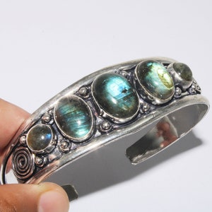 Pode incluir: Pulseira de bracelete de prata com quatro pedras ovaladas de labradorita. As pedras têm um brilho iridescente azul-esverdeado.