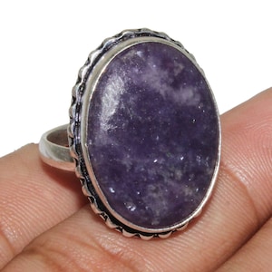 Op de afbeelding: Een zilveren ring met een grote ovale paarse edelsteen, gezet in een decoratieve zilveren zetting.