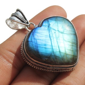 Puede incluir: Un colgante de plata en forma de corazón con una piedra preciosa de labradorita azul. El colgante tiene un borde de plata detallado.
