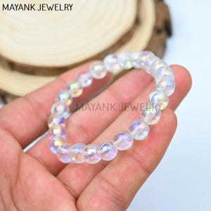 May include: A white iridescent crystal bracelet with round beads. The bracelet is made of natural stones and has a shimmering effect.