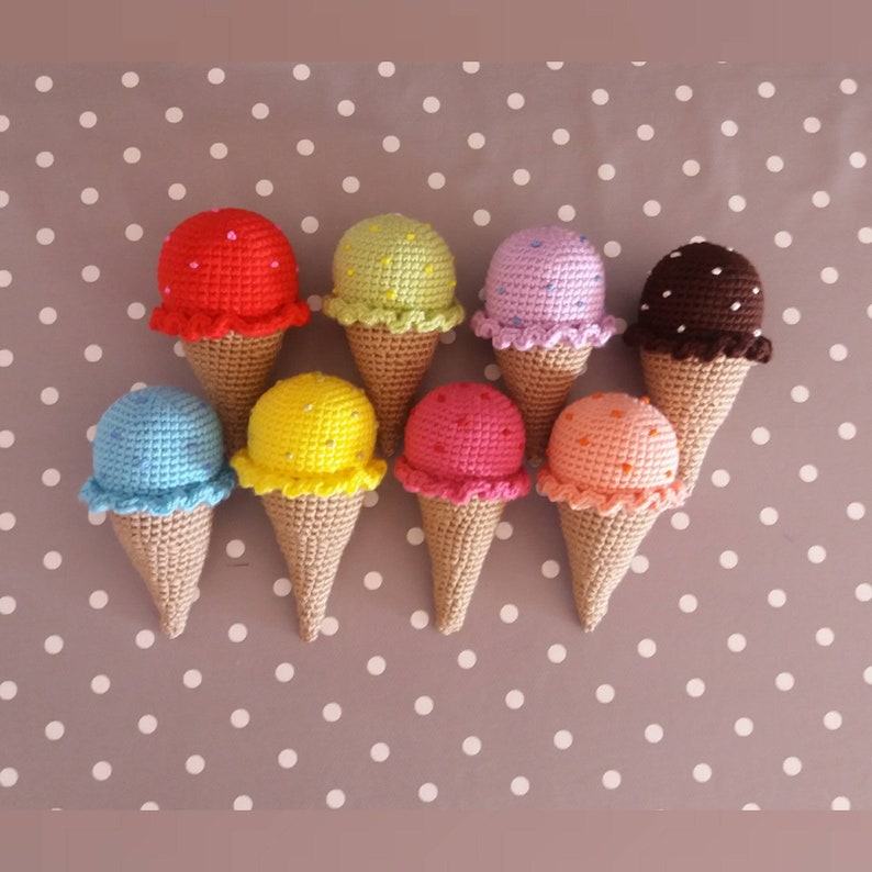 May include: Nine crocheted ice cream cones in various colors, including red, green, purple, brown, blue, yellow, pink, and orange. Each cone has a different colored ice cream scoop with sprinkles on top.