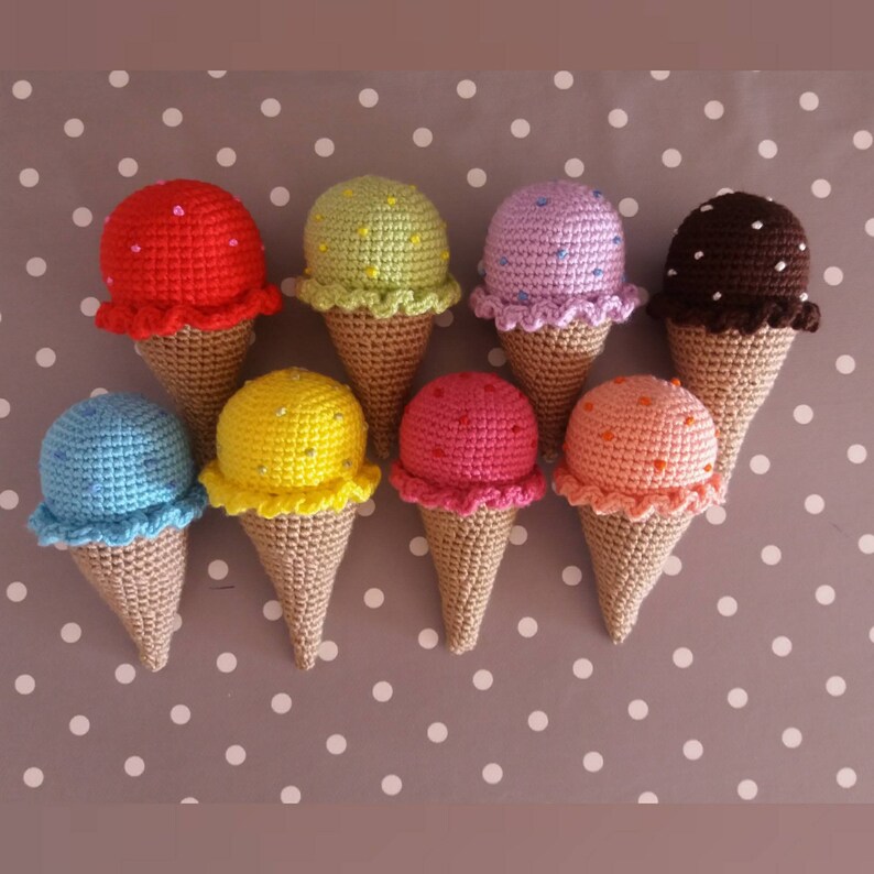 May include: Nine crocheted ice cream cones in various colors, including red, green, purple, brown, blue, yellow, pink, and orange. Each cone has a crocheted ice cream scoop on top with sprinkles.