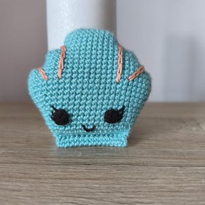 May include: A crocheted teal seashell with a smiling face and pink stitching.