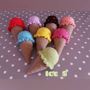 May include: Eight crocheted ice cream cones in various colors, including red, pink, purple, brown, orange, yellow, blue, and green. The cones are all decorated with white sprinkles and have a brown crocheted cone.