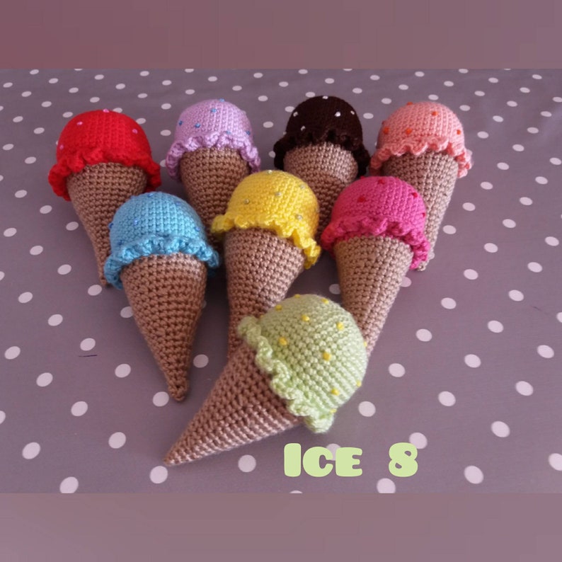 May include: Eight crocheted ice cream cones in various colors, including red, pink, purple, brown, orange, yellow, blue, and green. The cones are all decorated with white sprinkles and have a brown crocheted cone.