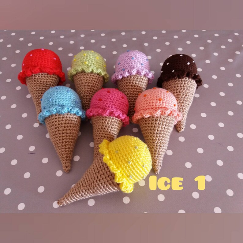 May include: A collection of eight crocheted ice cream cones in various colors, including red, green, purple, brown, blue, pink, orange, and yellow. The cones are arranged in a circle on a gray and white polka dot background. The text "ICE 1" is visible in the lower right corner of the image.