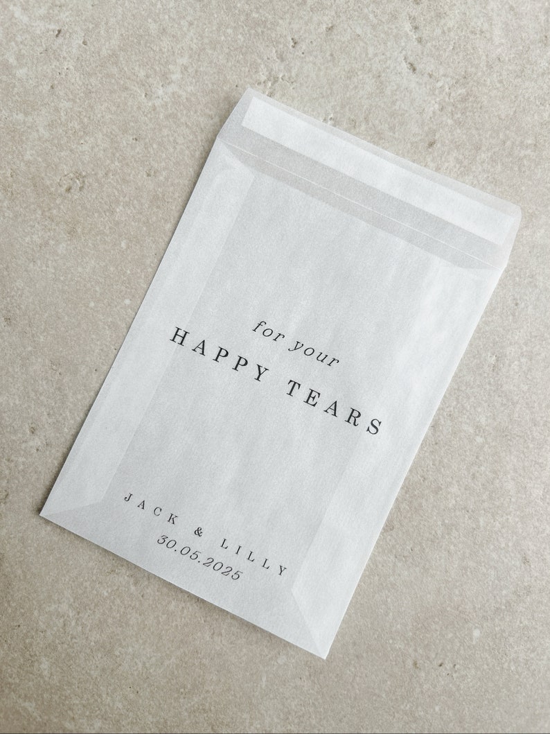 May include: White paper envelope with the text "for your HAPPY TEARS" and "JACK & LILLY 30.05.2025" printed on it.