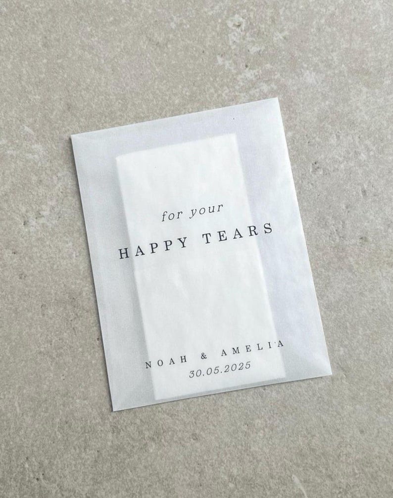 May include: White tissue paper envelope with the text "for your HAPPY TEARS" and "NOAH & AMELIA 30.05.2025" printed in black.
