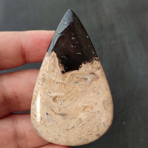 May include: A teardrop-shaped cabochon with a black and white agate pattern. The top half of the stone is black with white swirls, and the bottom half is white with brown swirls.