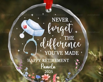 May include: A clear, round ornament with a red ribbon. The ornament features a nurse's cap and stethoscope illustration, with the text "NEVER forget the difference YOU'VE MADE." It also says "HAPPY RETIREMENT Pamela 2025" with floral accents.