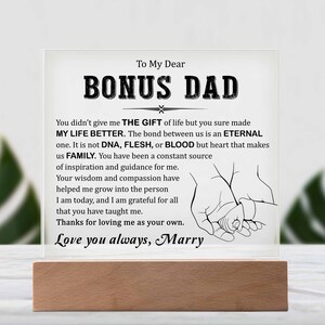 May include: A clear acrylic plaque with a wooden base, featuring a heartfelt message to a bonus dad. The message reads "To My Dear Bonus Dad You didn't give me the gift of life but you sure made my life better. The bond between us is an eternal one. It is not DNA, flesh, or blood but heart that makes us family. You have been a constant source of inspiration and guidance for me. Your wisdom and compassion have helped me grow into the person I am today, and I am grateful for all that you have taught me. Thanks for loving me as your own. Love you always, Marry"