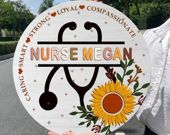 May include: A white wooden round sign with a brown stethoscope and sunflower design. The sign says "Nurse Megan" and has the words "Caring, Smart, Strong, Loyal, Compassionate" around the edge.