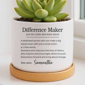 May include: White ceramic planter with a succulent plant. The planter has the text "Difference Maker (DIF-ER-UHNS MEY-KER) NOUN" and a definition. The planter also has the text "See also: Samantha".
