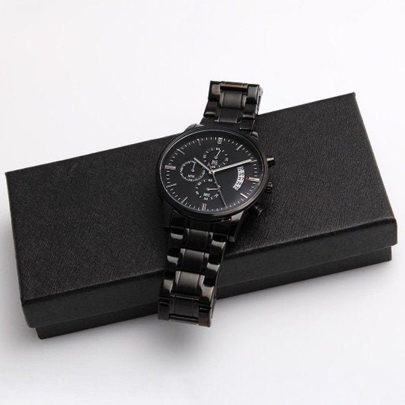 May include: A black chronograph wristwatch with a black leather strap and a black box. The watch has a date window and a silver face with black hands and markers.