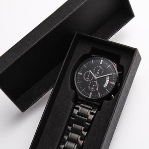 May include: A black chronograph wristwatch with a black metal strap in a black velvet box.