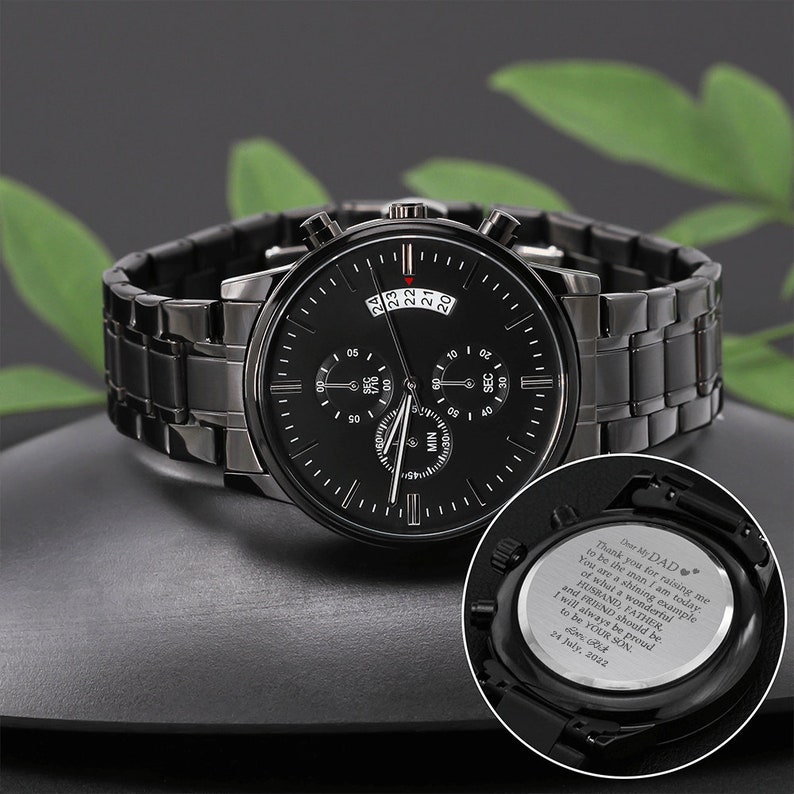 May include: A black chronograph watch with a stainless steel strap. The watch face has a black background with white markings and a date window. The back of the watch has an engraved message that reads "Dear My DAD, Thank you for raising me to be the man I am today. You are a shining example of what a wonderful Husband, Father, and Friend should be. I will always be proud to be your son. 24 July, 2022."