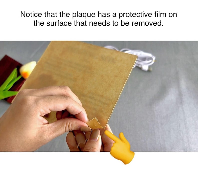 May include: A close-up of a hand peeling back a protective film from a brown plaque. The film is being peeled back from the top right corner of the plaque. The text "Notice that the plaque has a protective film on the surface that needs to be removed." is visible above the image.