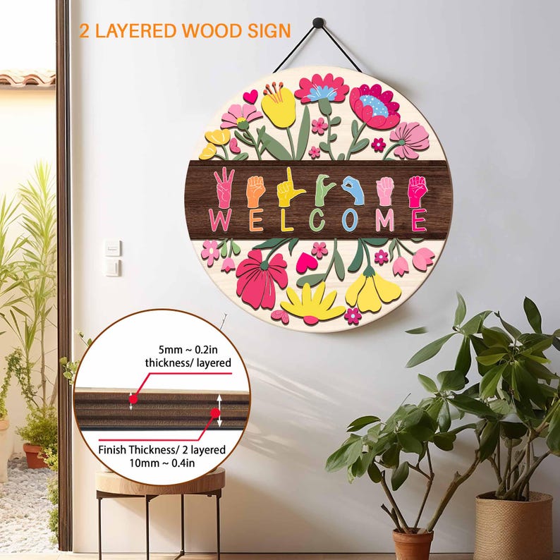 May include: A round, layered wooden sign with a floral design and the word "WELCOME" spelled out in colorful letters and hand gestures. The sign is approximately 10mm or 0.4 inches thick and is designed to hang. The sign has a cream background with colorful flowers.