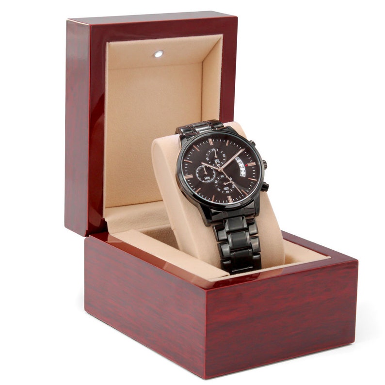 May include: A black chronograph watch with a rose gold face and date window, displayed in a dark red wooden box with a beige interior.