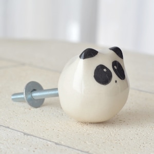 Op de afbeelding: Witte keramische pandabeer-deurknoppen met zwarte ogen en oren. De knop heeft een zilveren schroef.