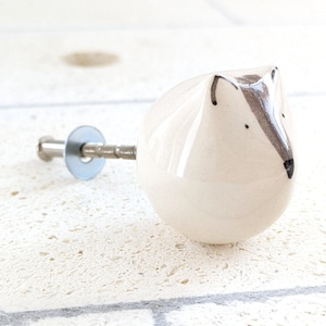 Può includere: Pomo per armadio in ceramica bianca con un design di volpe grigio e nero dipinto a mano. Il pomo ha una vite argentata.